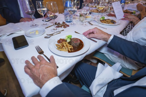 Steak with vegetables and pasta in an elegant table setting with white wine glasses and cloth napkins