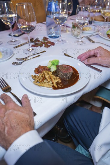 Steak with vegetables and pasta in an upscale dining environment with white tablecloth and wine glasses