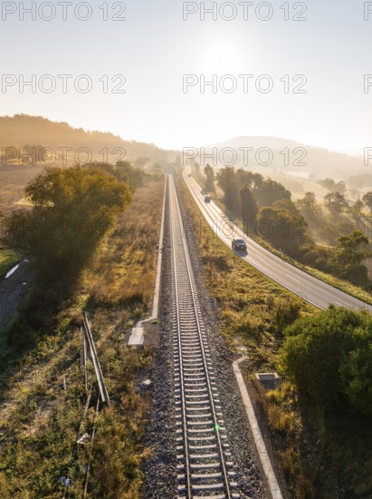 View of railway tracks and country road in the early morning light. Trees and fields frame the track, gentle fog in the background, Hermann Hesse railway, Ostelsheim, Black Forest, Germany