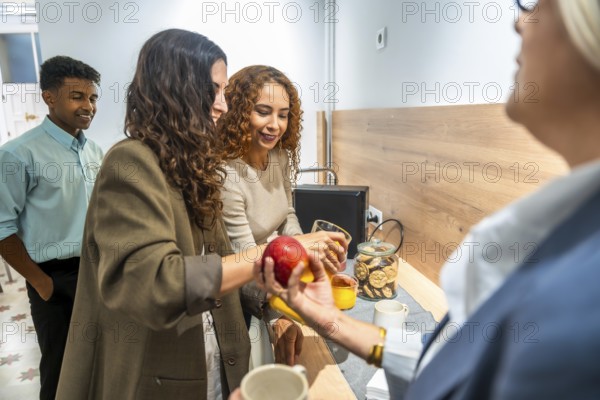 Coworkers gathering around a counter, offering an apple and orange juice, fostering team building and collaboration in a diverse and inclusive office environment during a light snack break