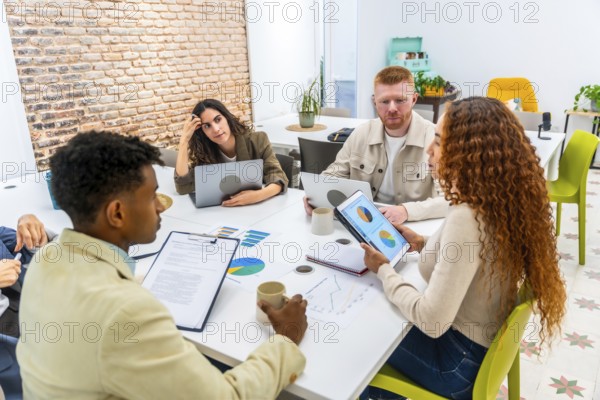 Diverse business professionals collaborating around a conference table in a modern office, reviewing data, charts and tablets while planning strategy, brainstorming and making decisions
