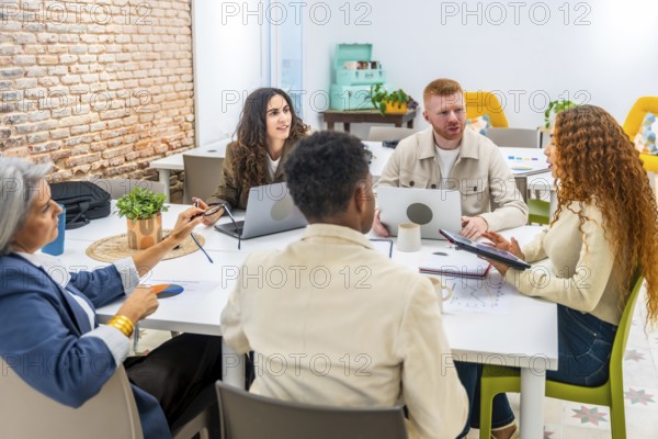 Diverse business professionals working together around a table, sharing ideas and analyzing data with laptops and a tablet during a business meeting in a modern office space