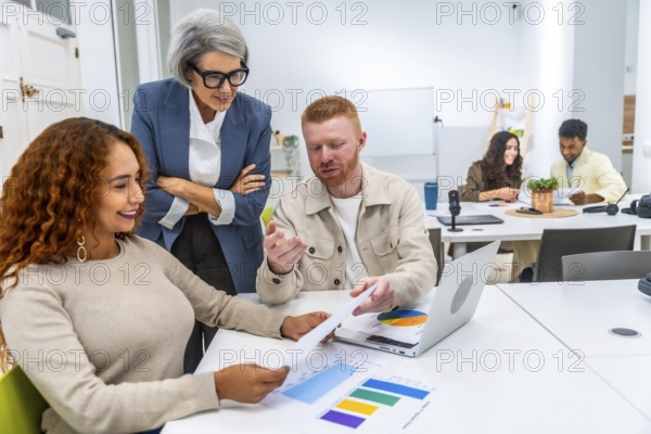 Multigenerational business team discussing charts and data with laptop in a modern coworking office, presenting a scene of teamwork and cooperation among diverse employees
