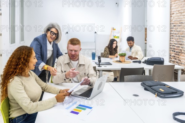 Diverse business people collaborating around a table in a modern office, discussing data and working together on projects, fostering a dynamic spirit of teamwork