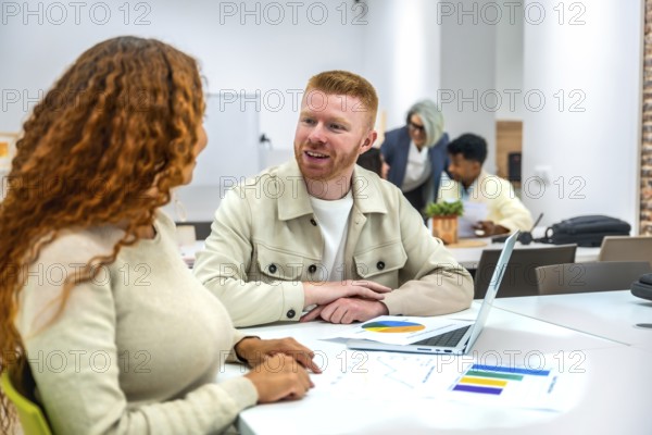 Diverse colleagues collaborate over charts and laptops in a modern coworking space, sharing ideas, analyzing data and planning strategy during an informal, creative meeting