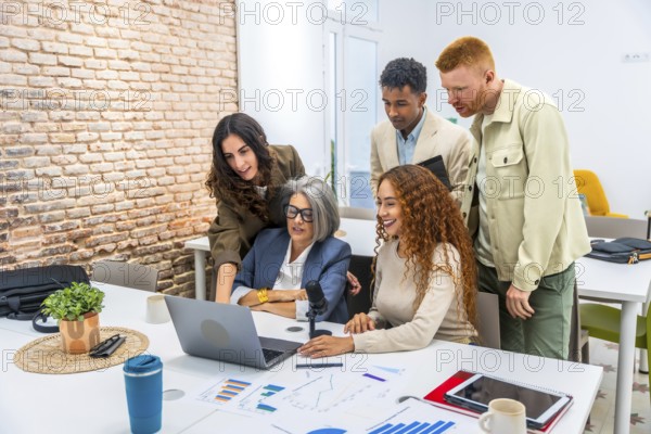 Diverse business professionals working together around a laptop, analyzing financial charts and presenting ideas during a casual office meeting, showcasing teamwork and modern communication