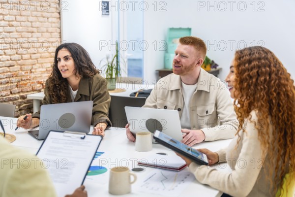 Diverse team of young entrepreneurs actively collaborating and exchanging ideas around a table with laptops and documents during a creative business meeting in a modern office space