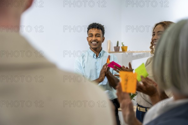 Diverse business people actively participating in a creative brainstorming session, discussing new ideas and holding colorful sticky notes in a modern office environment
