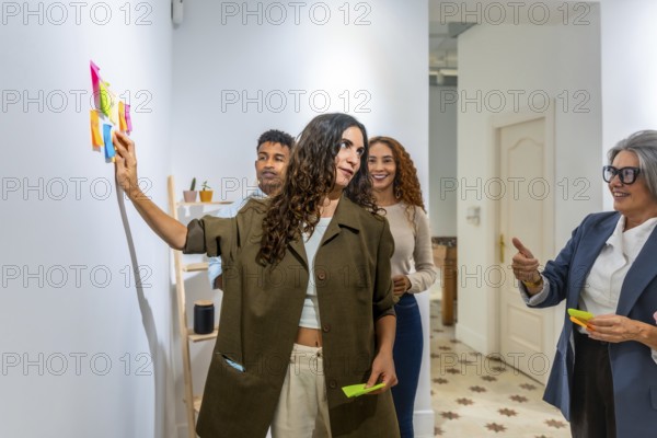 Diverse business team collaborating and brainstorming ideas, using colorful sticky notes on a wall during a creative strategy meeting in a modern office environment