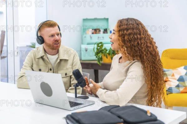 Diverse man and woman hosting a podcast, looking at each other while discussing topics and interviewing, utilizing a microphone, laptop, and headphones for the live recording