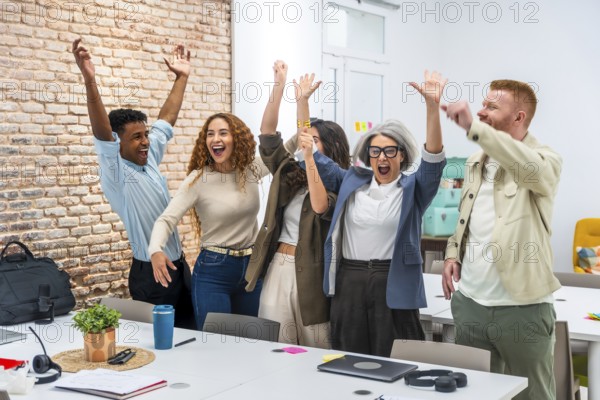 Multiracial business team in a modern office cheering with arms raised, celebrating a shared success and energized by teamwork, collaboration and accomplishment