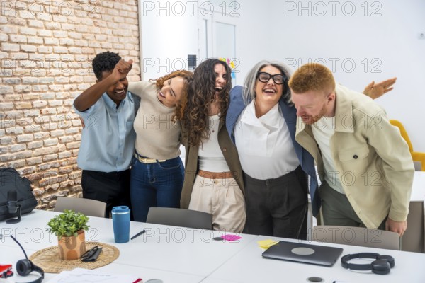 Diverse business team embracing each other excitedly, laughing and celebrating success together in a modern office meeting room, showing strong teamwork and positive corporate culture