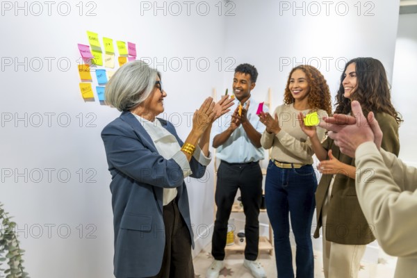 Diverse business people clapping hands in an office meeting room, celebrating a successful project achievement or a senior female manager's accomplishment, demonstrating teamwork and appreciation