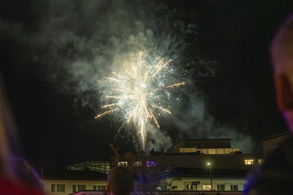 Colourful fireworks light up the night sky over a dark building complex with spectators, Fire Night, Sindelfingen, Germany