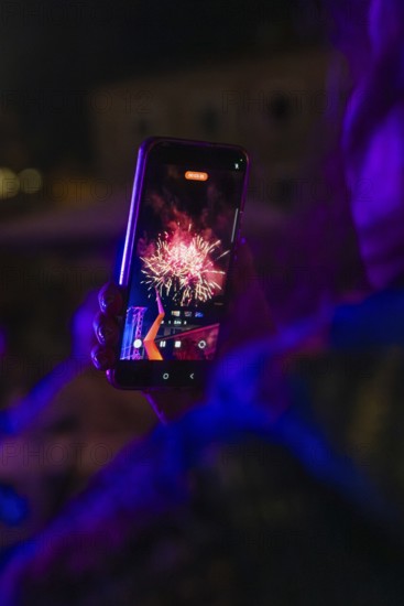 Person holding a mobile phone showing a photo of colourful fireworks at night, Fire Night, Sindelfingen, Germany