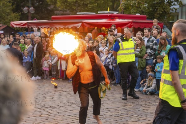 A fire eater entertains a crowd on a cobbled street in front of red stalls, Fire Night, Sindelfingen, Germany