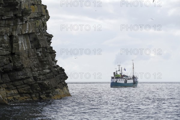 Turquoise boat on open sea near rocky cliffs, cloudy sky, Isle of Noss, Shetland Islands, Scotland, United Kingdom