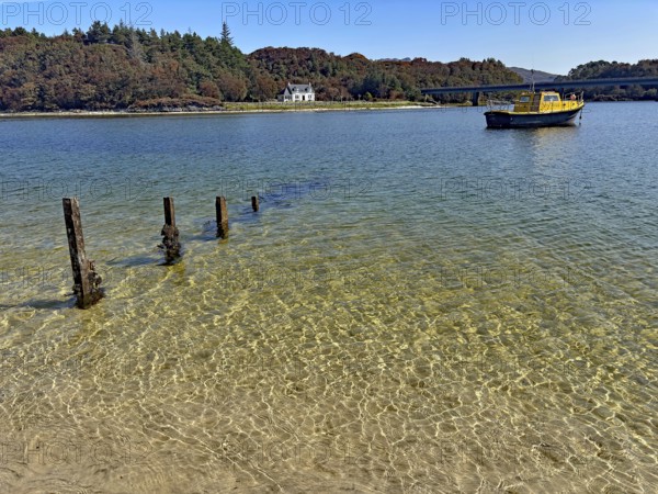 Clear lake surface with a yellow boat and wooden houses on the shore, Silver Sands of Morar, Morar, Scotland, United Kingdom