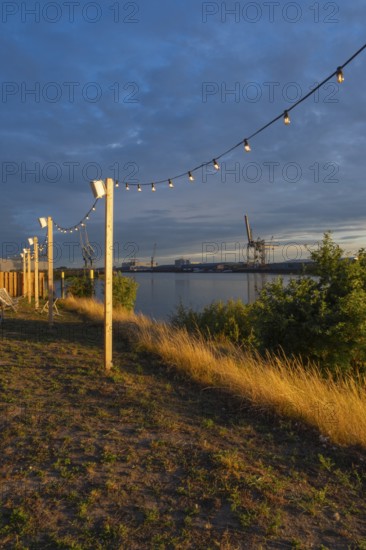 View from the outside area of a restaurant at Lankenauer Höft through a string of lights onto Neustadt harbour in the evening light, Weser, Bremen, Germany