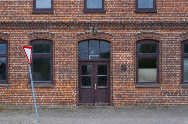 View of the entrance area of a brick building with a leaning traffic sign in front of it, Uenzen, Bruchhausen-Vilsen, Lower Saxony, Germany