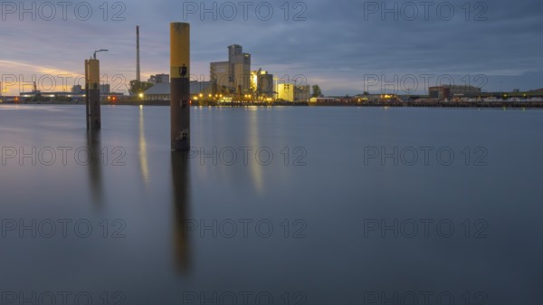 View across the Weser past dolphins to an industrial area in the evening light, Gröpelingen, Bremen, Germany