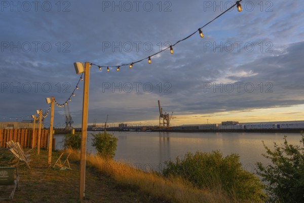 View from the outside area of a restaurant at Lankenauer Höft through a string of lights onto Neustadt harbour in the evening light, Weser, Bremen, Germany