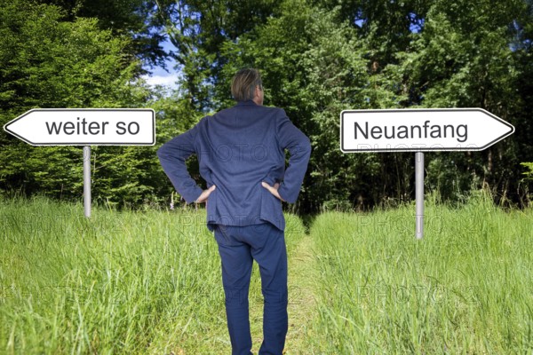 (Photomontage) Businessman stands in nature and has the choice between the direction CONTINUE AS IS and the direction NEW BEGINNING
