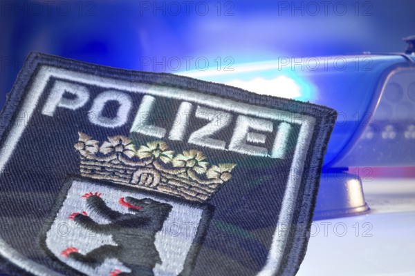 (Photomontage) Symbolic image of a police operation in Berlin: Berlin police emblem in front of flashing blue lights