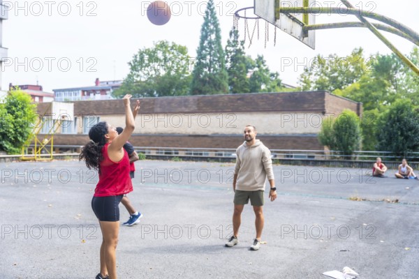 Young woman practicing basketball shooting at the hoop under the supervision of her coach on an outdoor court, embodying dedication and athleticism