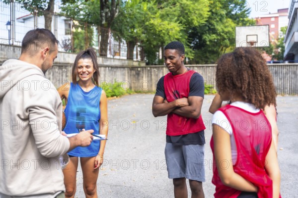 Coach holding clipboard and talking to multi ethnic basketball team players during training session on outdoor court, focusing on teamwork and game strategy