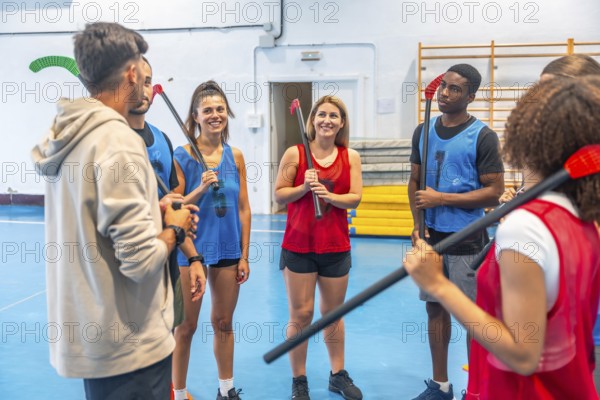 Multi ethnic team players actively listening to their coach as they receive instructions during a dynamic floorball training session inside a spacious gymnasium