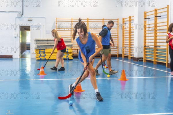 Floorball players running and practicing their stick handling skills during a training session inside a gymnasium, focusing on agility and precision with colorful cones marking the course