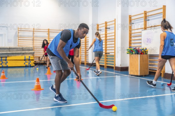 Focused young athlete dribbling floorball ball in gym, practicing stick handling skills with teammates during training session, showcasing agility and precision