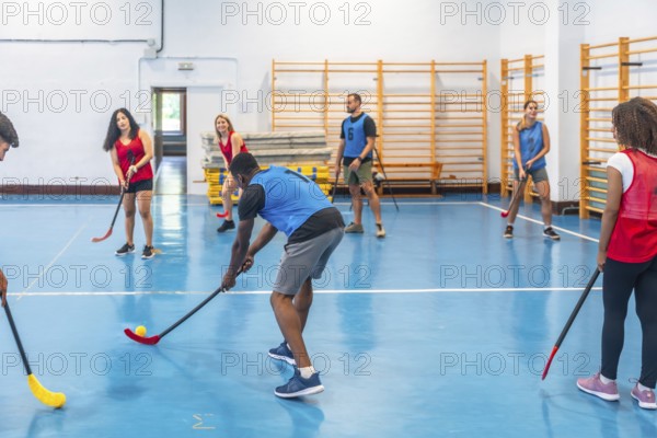 Floorball team players practicing passes during training inside a gym, skillfully hitting the ball with their sticks on the vibrant blue floor, showcasing teamwork and athleticism