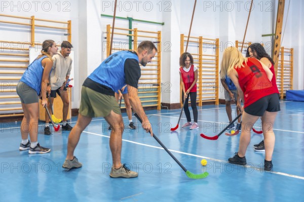 Two floorball teams wearing colorful sportswear are practicing passes and shots in a gymnasium, showcasing teamwork and athleticism during training