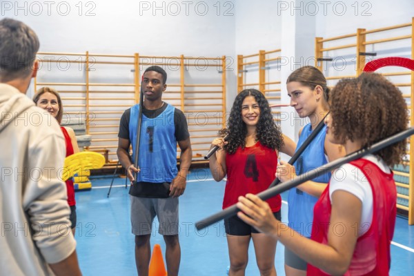 Multi ethnic floorball team gathered in a gym, attentively listening to their coach's instructions during an intense training session focused on improving skills and teamwork