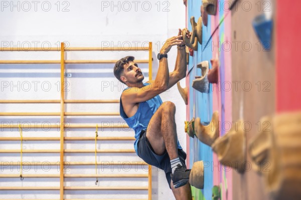Young male athlete practicing sport climbing on a colorful indoor climbing wall, demonstrating strength, agility, and focus in a gym environment