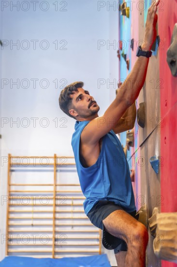 Concentrated male athlete meticulously gripping colorful handholds while ascending an artificial rock climbing wall, demonstrating strength, agility, and focus in an indoor gym environment