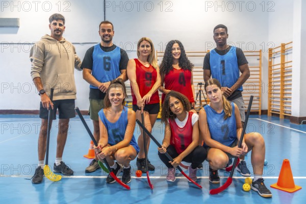 Multi ethnic floorball team posing together with their sticks in gymnasium after training session, demonstrating team spirit and sportsmanship