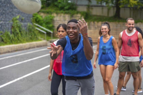 Male rugby player wearing a blue training bib is catching a ball during a practice session, surrounded by his smiling teammates on an outdoor court