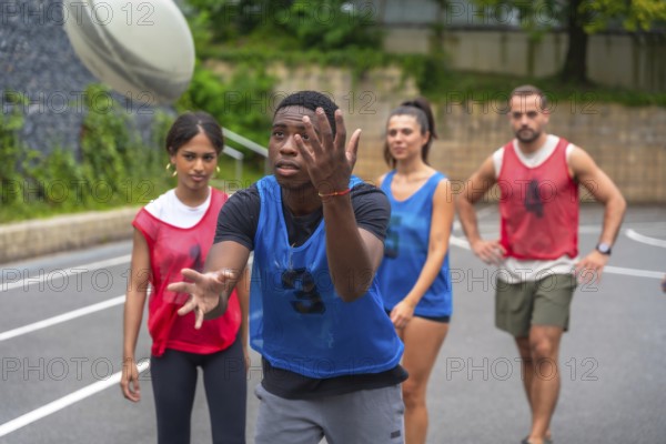 Rugby player wearing a blue training bib is catching a ball during practice, surrounded by teammates wearing red training bibs on an outdoor court