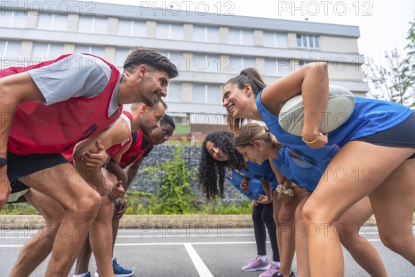 Two rugby teams, one in red and one in blue, are facing each other and smiling before a match, with a female player holding the ball under her arm
