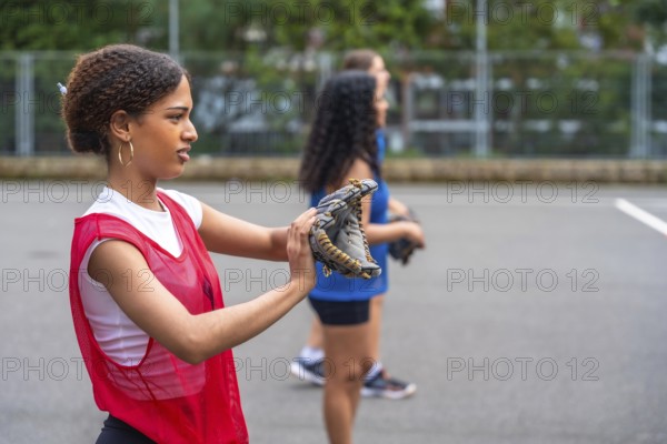 Young woman baseball player putting on her glove, preparing for practice with teammates under the warm sun, embodying the spirit of teamwork and dedication on the field