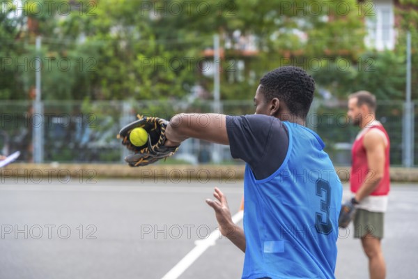 Young baseball player wearing a blue uniform is pitching the ball with his glove during a game on the field while another player waits in the background