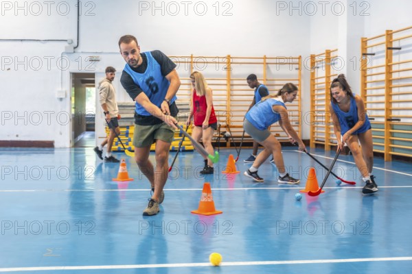 Group of athletes engaged in an intense floorball training session, skillfully dribbling the ball with their sticks and navigating between cones in a vibrant gym environment