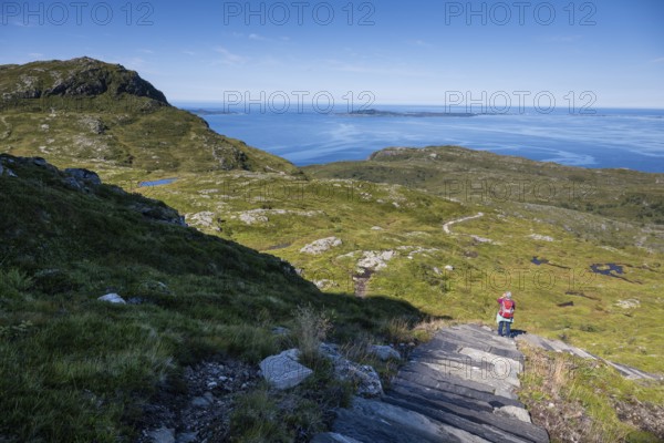 Woman with backpack standing on stone stairs, Sherpat stairs or Midsund stairs or Midsundtrappene, Bløkallen hike, in the background sea and islands, island Otroya or Otrøya, Møre og Romsdal, Norway