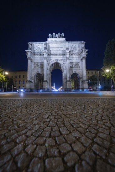 Night shot of the illuminated Siegestor on cobblestone street, Siegestor, Munich, Germany