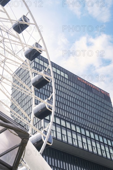 Modern Ferris wheel near a glass building under a blue sky, Werksviertel Munich, Munich, Germany