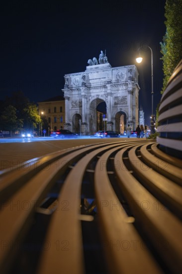 Siegestor at night with bench in the foreground and street lights, Siegestor, Munich, Germany