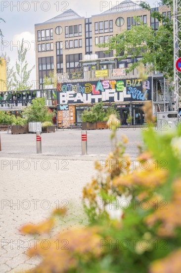 Building with urban graffiti 'Nothing Lasts But the Beautiful' and flowers, Werksviertel Munich, Munich, Germany